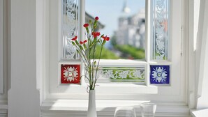 A table with a vase of red flowers, a book, and two glasses of white wine by a window with decorative glass panes. - ROEWERS Privathotel & Spa (Sellin)