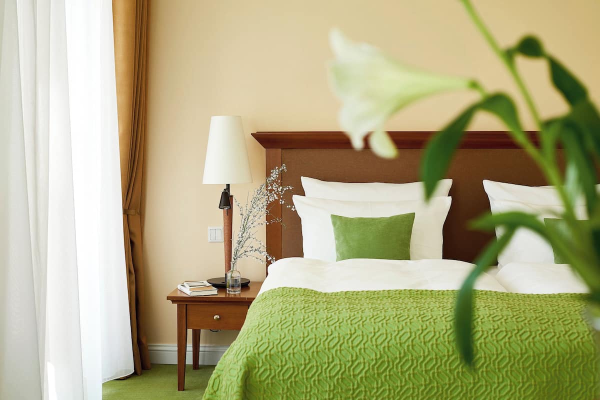 A hotel room with a bed, a nightstand, a lamp, and a vase with flowers.