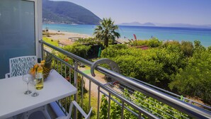 A balcony with a table, two wine glasses, and a bottle of wine. The view includes a beach, clear blue sea, and distant mountains. - Nefeli (Lefkada)