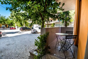 Un balcón con mesa y sillas, una planta en maceta y vista a una calle con coches aparcados y edificios.