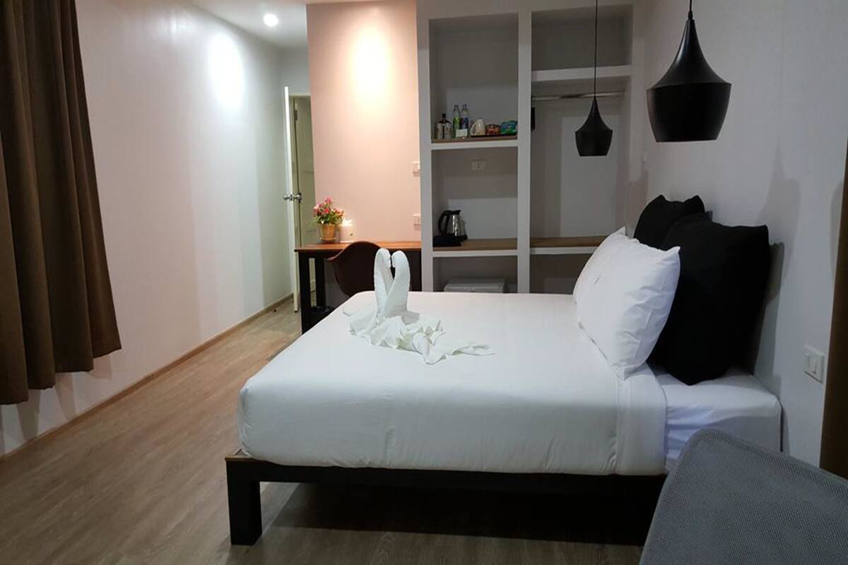 Quarto de hotel com cama, escrivaninha, guarda-roupa e luminária suspensa.