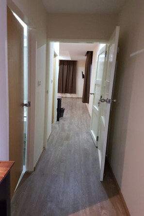 A hallway with a wooden floor, a door on the left, and a glass door on the right.