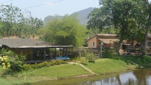 A riverside property with a thatched-roof structure, a small dock, and a house with a sloped roof. - Narinfah Resort (Kaeng Krachan)