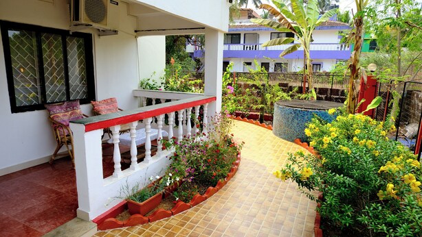 A covered outdoor area with a white railing, a bench, and potted plants. - Sea Pearl Guest house (Candolim)
