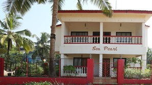 A two-story building named "Sea Pearl" with a balcony, surrounded by a red fence and palm trees. - Sea Pearl Guest house (Candolim)