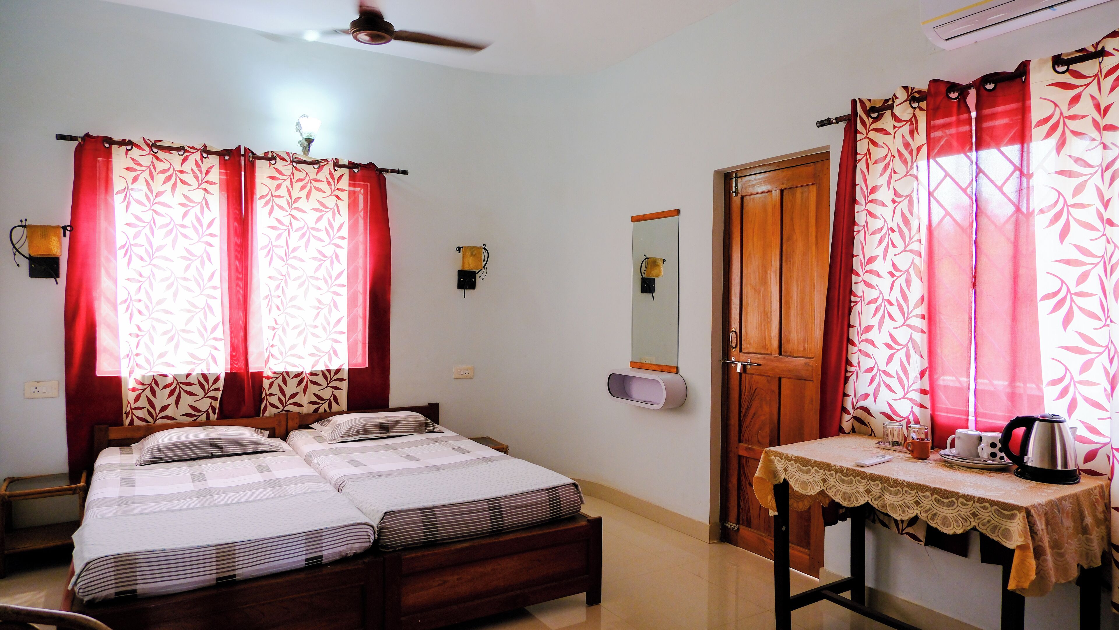 A bedroom with a bed, a bedside table with a kettle, and a wooden door.