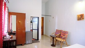 A room with a wooden door, a small table with a chair, a refrigerator, and a wall-mounted air conditioning unit. - Sea Pearl Guest house (Candolim)