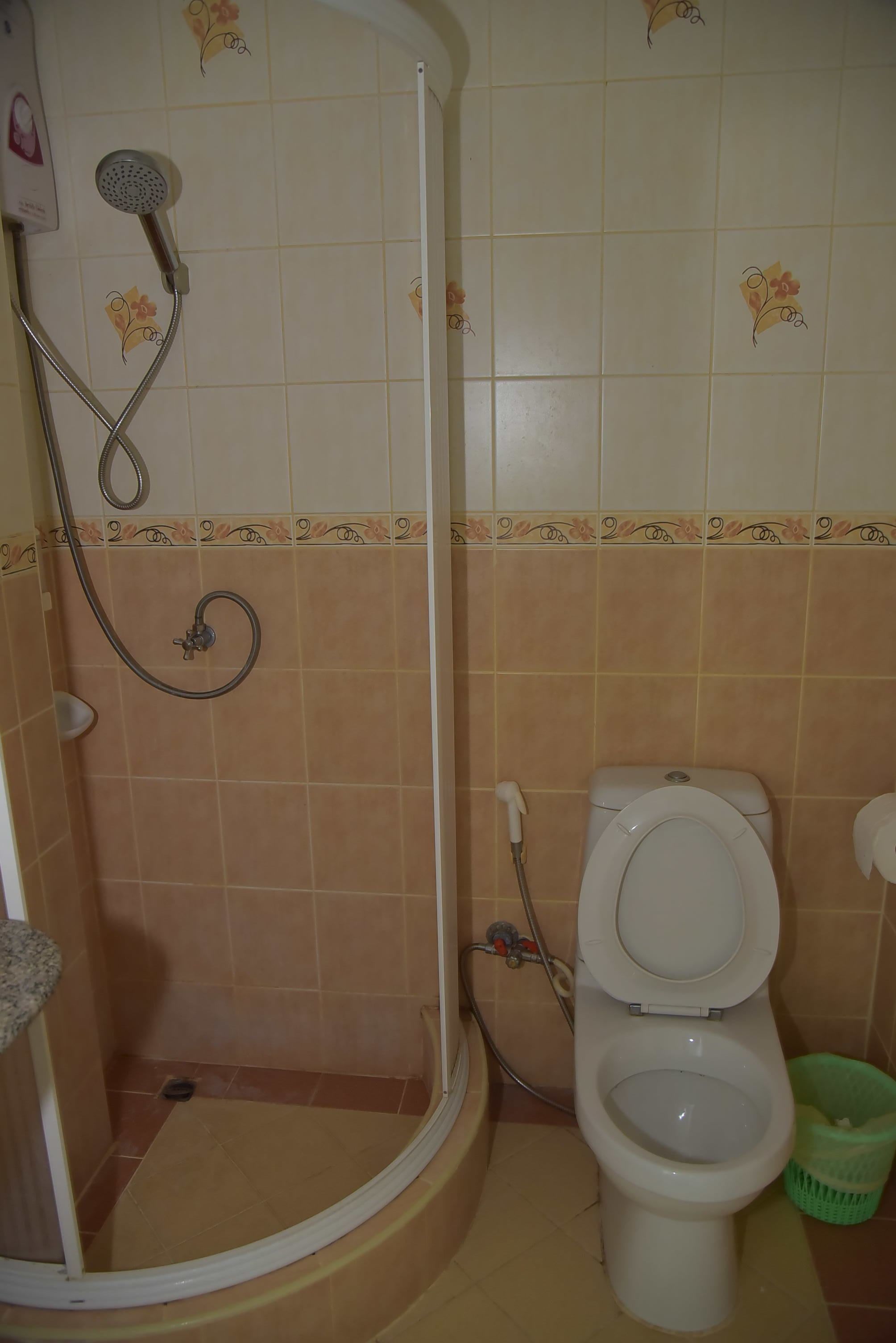 A bathroom with a shower, toilet, and a green trash bin.