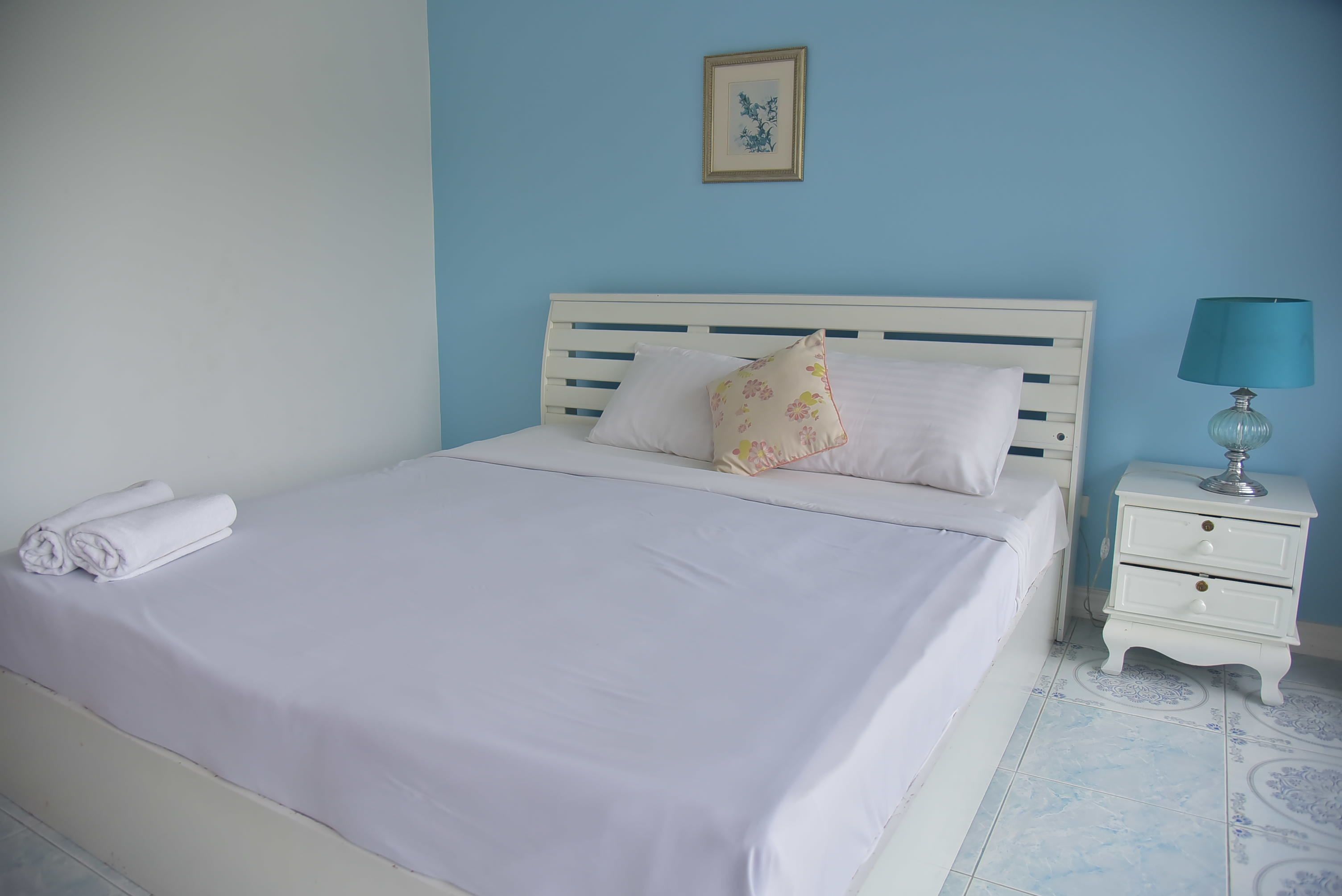 A neatly made bed with white linens, a white headboard, and a small bedside table with a lamp.