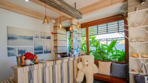 Zona de recepción con un mostrador de madera, un gran oso de peluche y una ventana con vistas a zonas verdes.