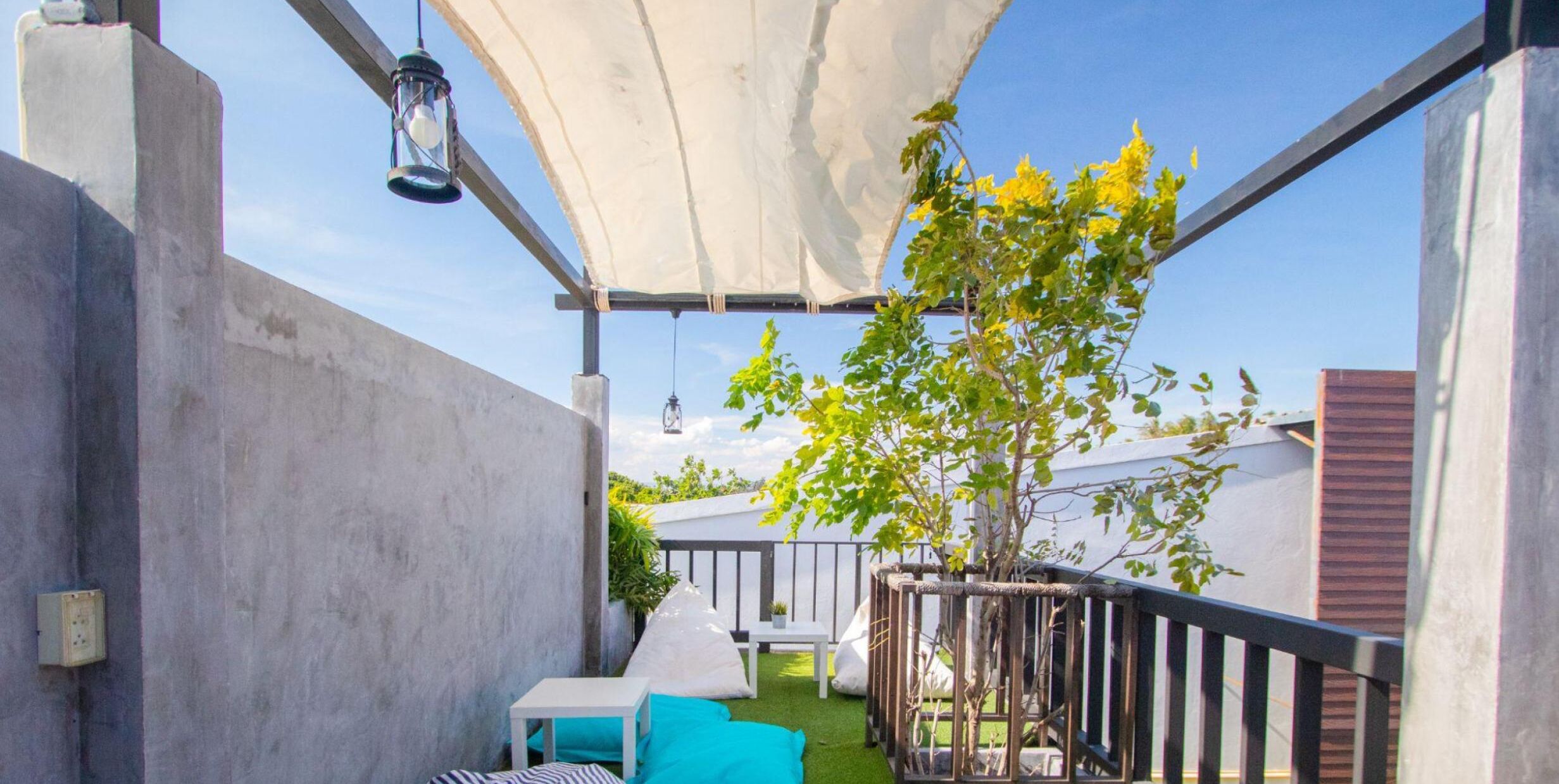 Un espace extérieur abrité, avec une table et des chaises blanches, une lanterne suspendue et un arbre.