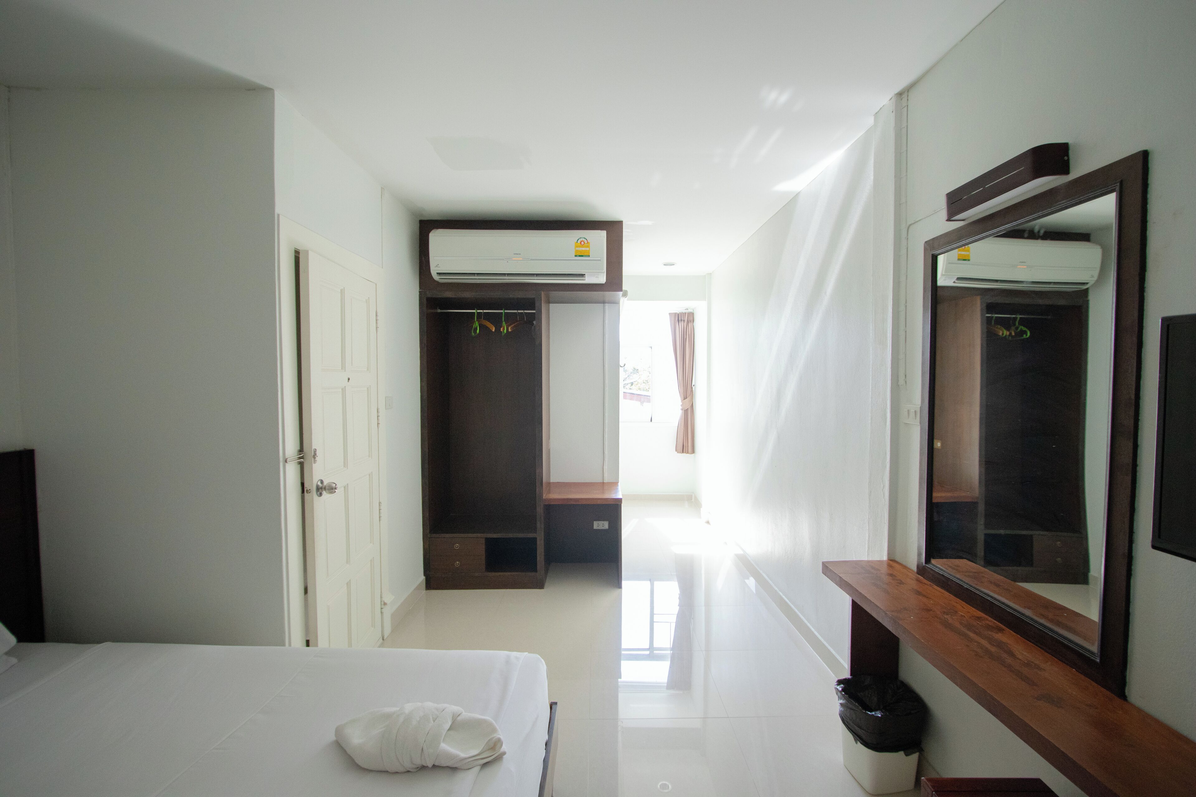Une chambre d’hôtel comprenant un lit, un banc en bois, un miroir, un appareil de climatisation et une armoire.