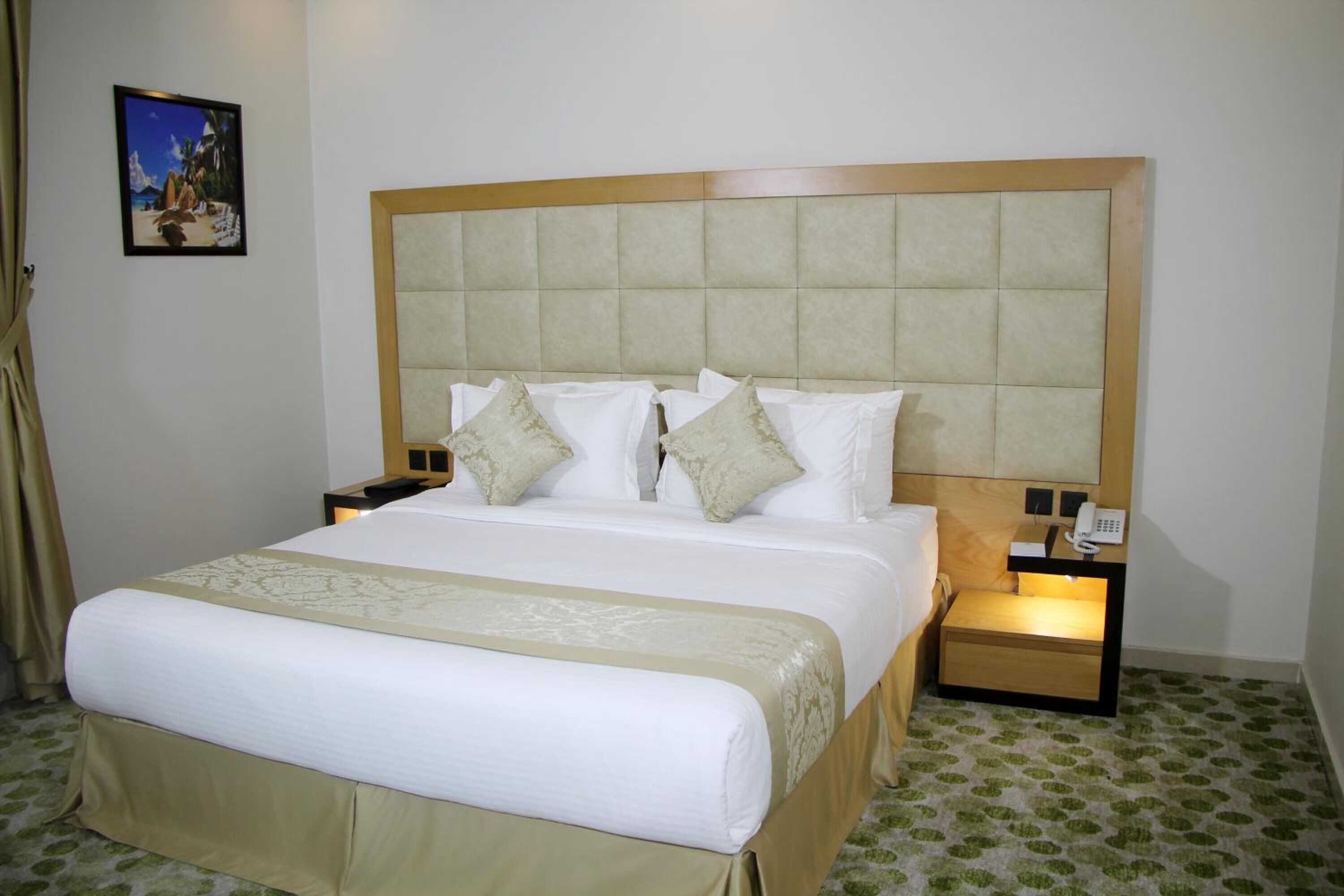 A hotel room with a large bed, a wooden headboard, two bedside tables with lamps, and a framed picture on the wall.