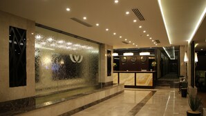 A hotel lobby with a reception desk, a decorative wall with a water feature, and a clean, polished floor. - AlMuhaidb Residence Al Khafji (Al Khafji)