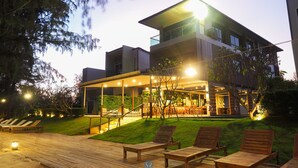 A modern two-story building with a covered outdoor area, wooden lounge chairs, and a well-lit garden. - Sea & Sea Villa Resort Sangaroon (Thap Sakae)