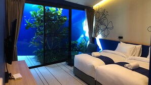 A hotel room with a bed, a desk, a large window with a view of greenery, and a wall with a floral design. - Sea & Sea Villa Resort Sangaroon (Thap Sakae)