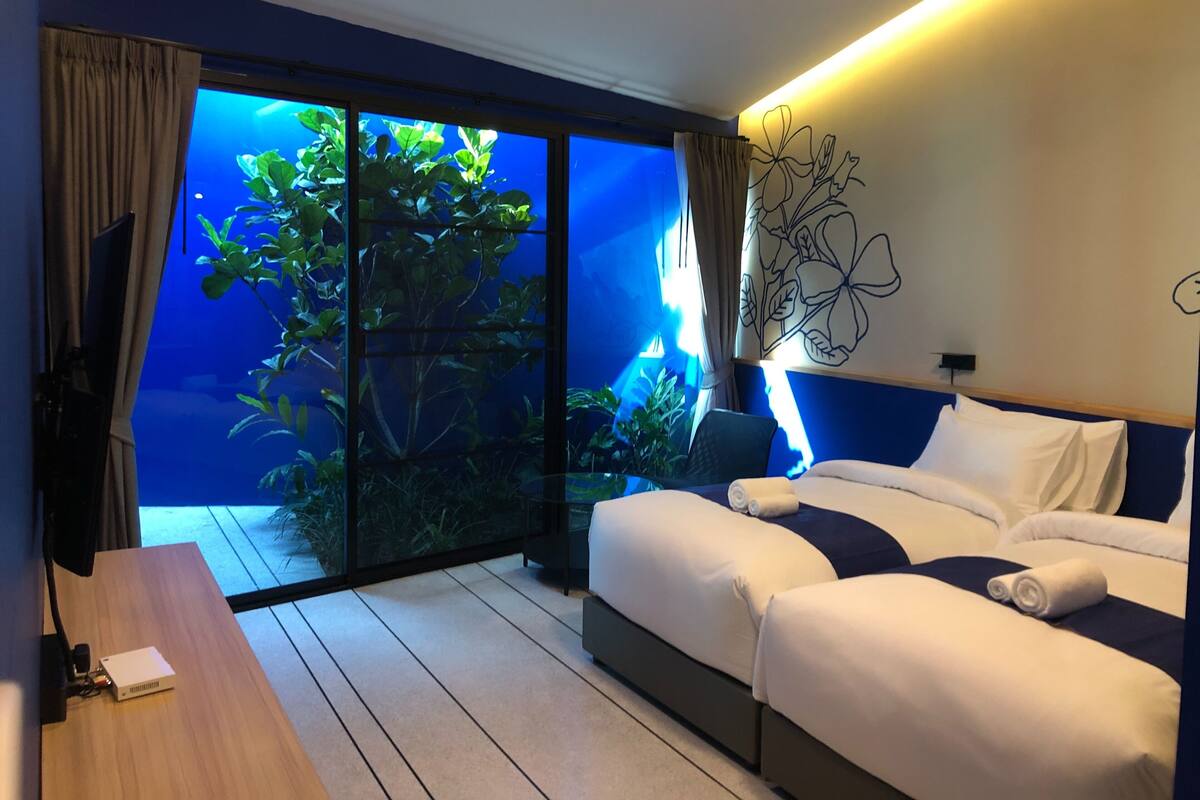 Une chambre d’hôtel comprenant un lit, un bureau, une grande fenêtre donnant sur un paysage verdoyant et un mur orné d’un motif floral.