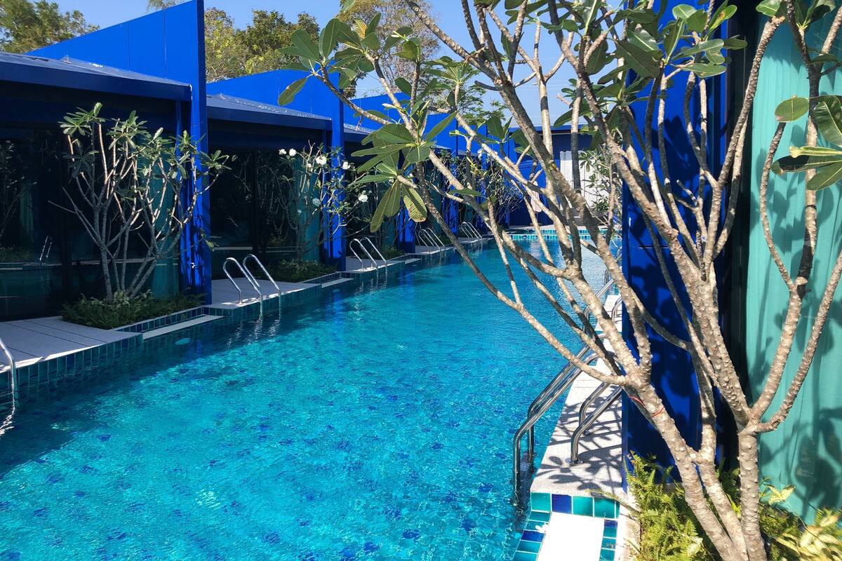 Une piscine à l’eau d’un bleu limpide, entourée de bâtiments bleus et de verdure.