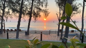 A sunset view from a deck overlooking a beach with lounge chairs and a wooden walkway. - Sea & Sea Villa Resort Sangaroon (Thap Sakae)