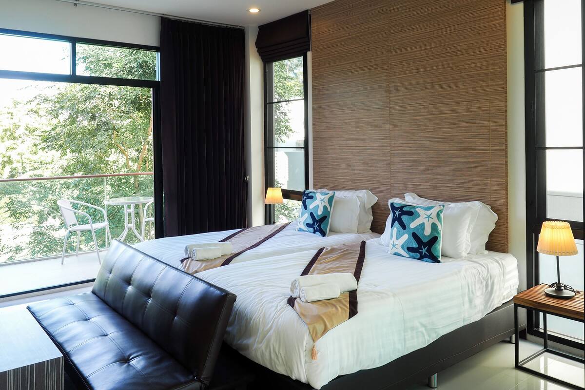Une chambre d’hôtel moderne avec un grand lit, un banc et une vue sur la verdure environnante.