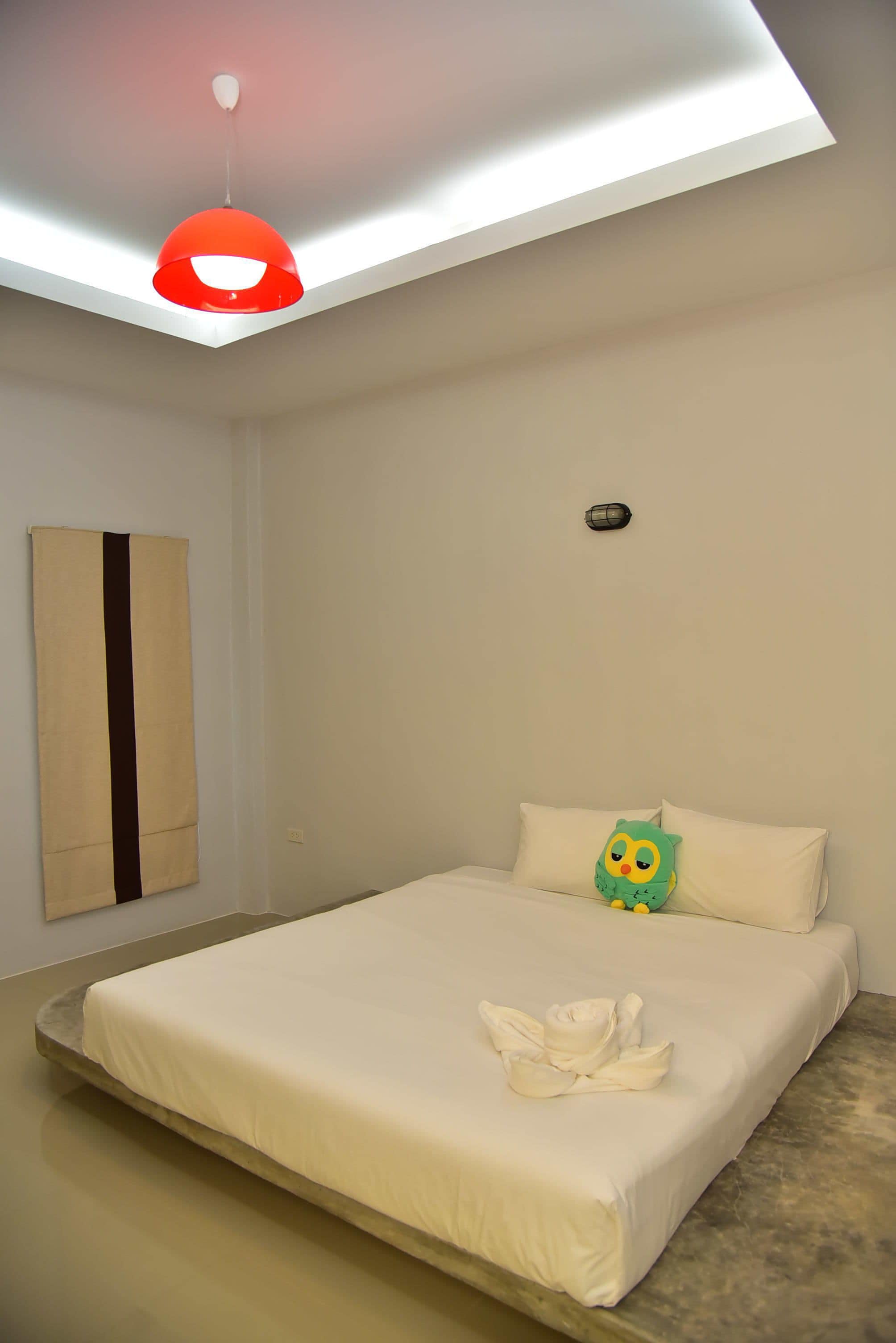 A bedroom with a bed, a hanging light fixture, a wall-mounted light, and a pillow with a cartoon character.