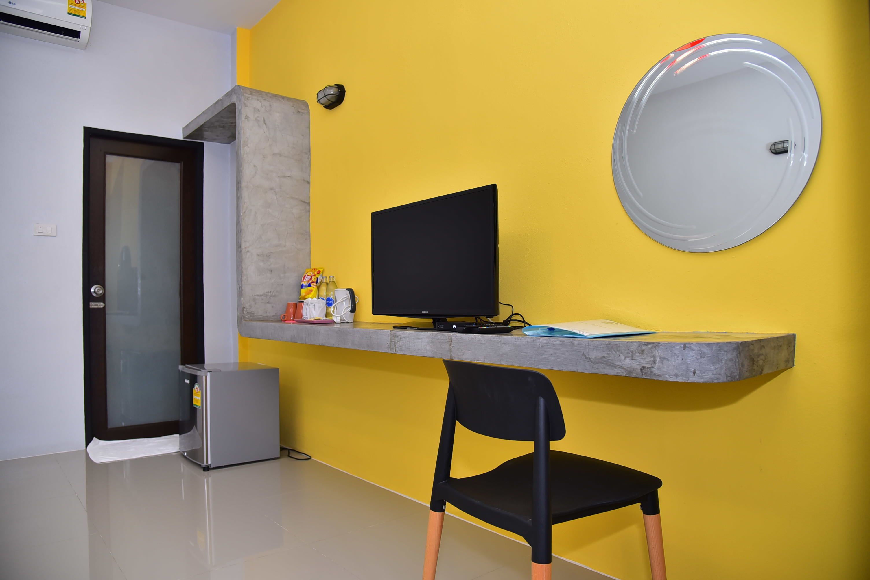 A room with a yellow wall, a black chair, a desk with a computer, and a small cabinet.