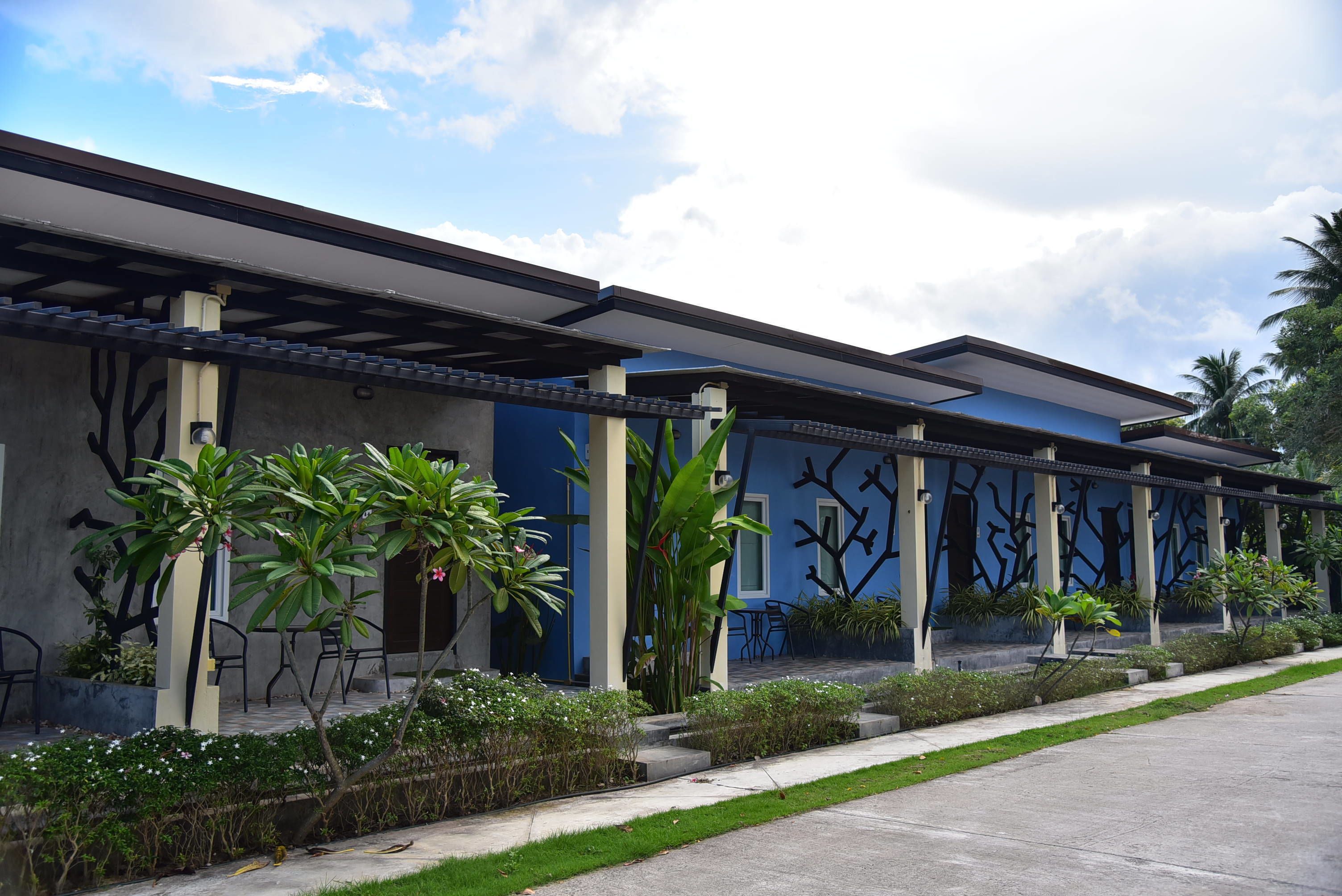 A modern building with a blue facade, outdoor seating, and greenery.