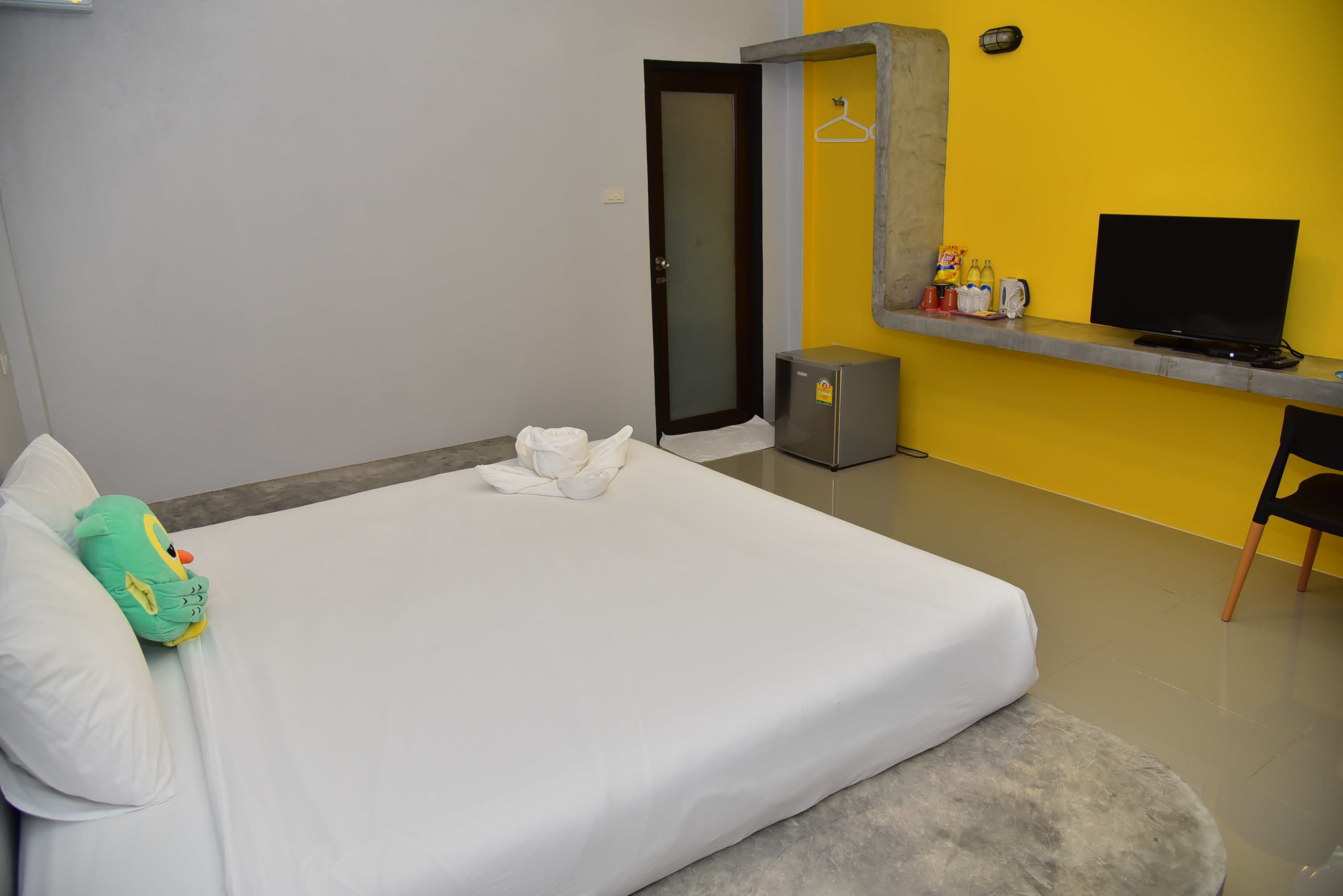 A hotel room with a bed, a grey bench, a television, and a small cabinet.