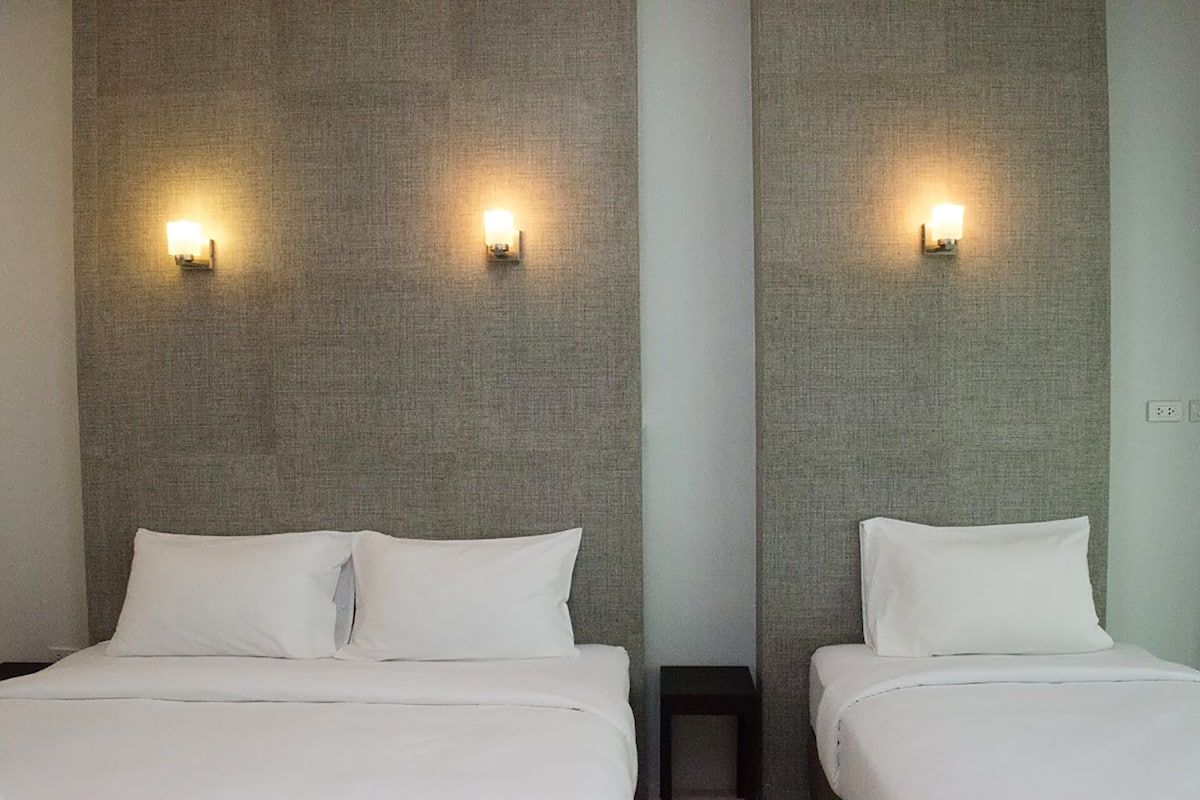 A hotel room with two beds, each with white linens and pillows. There are wall-mounted light fixtures on either side of the beds.