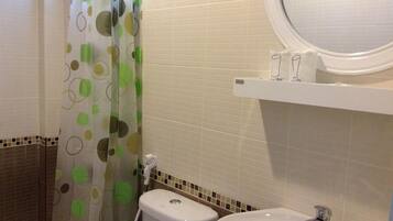 A bathroom with a toilet, bidet, and sink. There is a shower curtain with a green and brown pattern. The walls are tiled with a beige and brown color scheme.