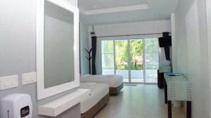 A modern hotel room with a large mirror, a sofa, a small table, and a view of greenery outside. - Bankrut Resort (Bang Saphan)