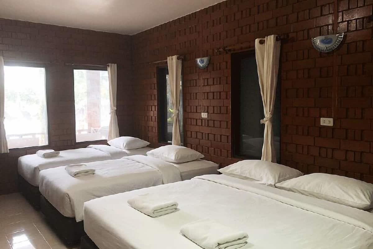 A hotel room with three beds, each with white linens and pillows, and a brick wall.