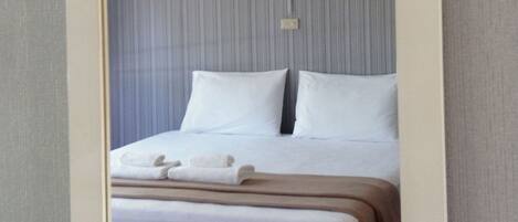 A neatly made bed with white linens and a brown blanket, a small bedside table with a white towel, and a wall with vertical stripes.