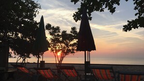 A beachside lounge with striped lounge chairs and umbrellas, overlooking the sea during sunset. - Bankrut Resort (Bang Saphan)