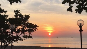 A sunset over a beach with a lamp post and foliage in the foreground. - Bankrut Resort (Bang Saphan)