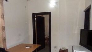 A small, sparsely furnished room with a wooden table, a single chair, a television, and a refrigerator. - Prumssy Hotel (Lekki)