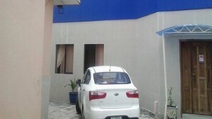A white car parked in a narrow driveway with a blue awning and a wooden door. - Prumssy Hotel (Lekki)