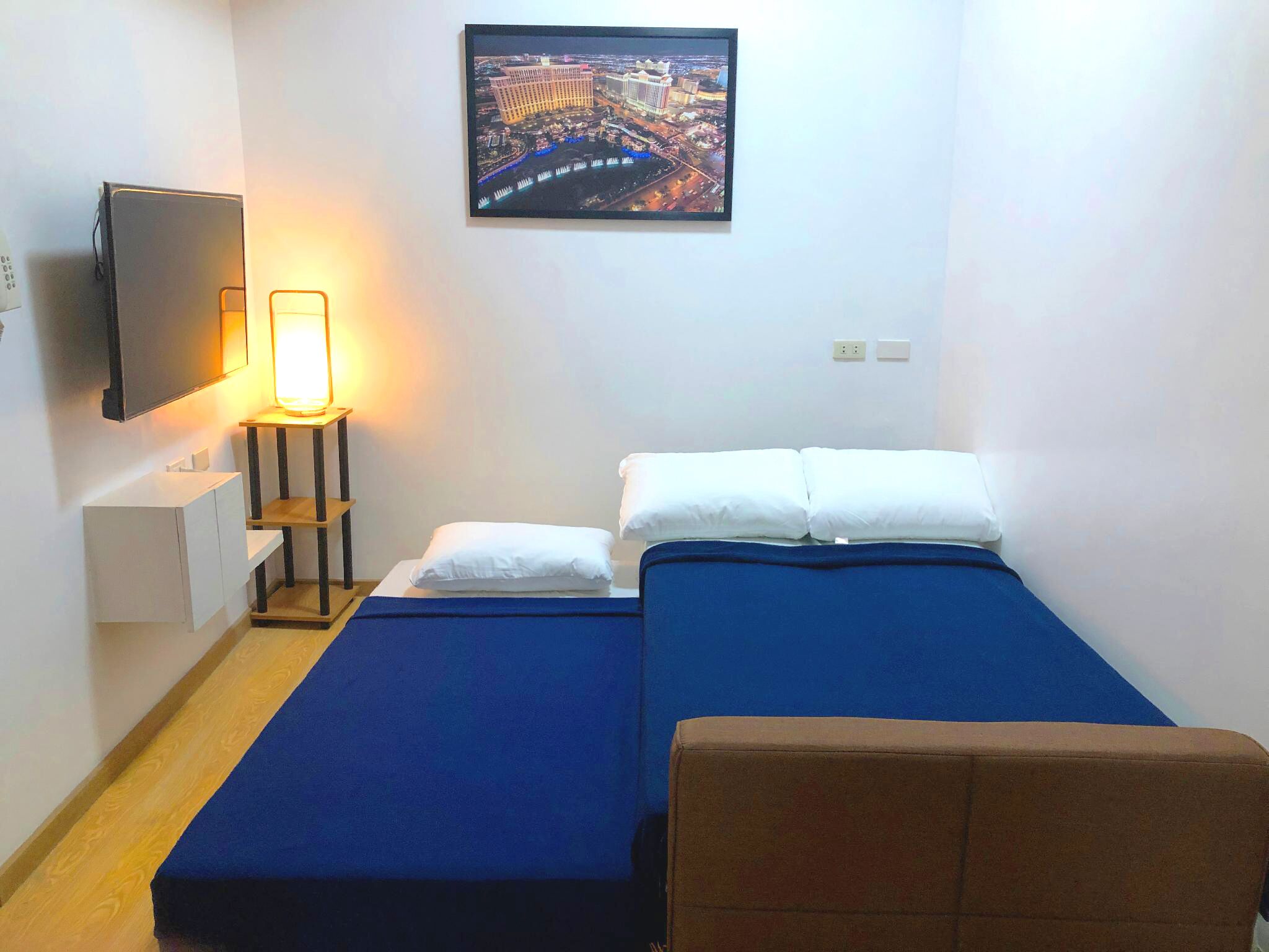 A small, neatly arranged hotel room with a bed, a chair, a desk, and a TV mounted on the wall.