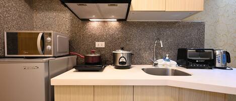A kitchen with a microwave, toaster, and slow cooker on the counter, a sink, and wooden cabinets.
