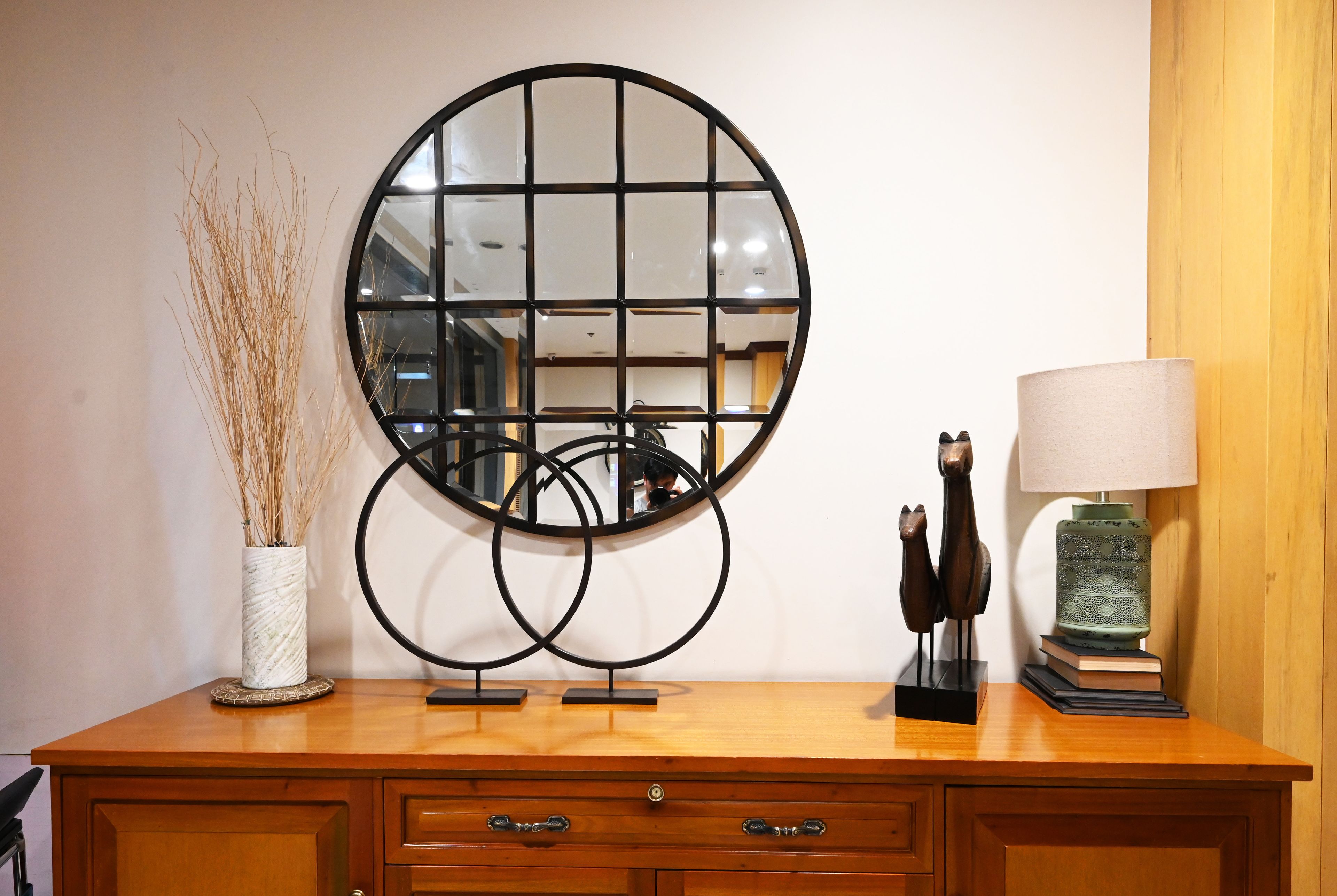 A wooden dresser with a mirror, a vase with dried plants, a lamp, and decorative items.
