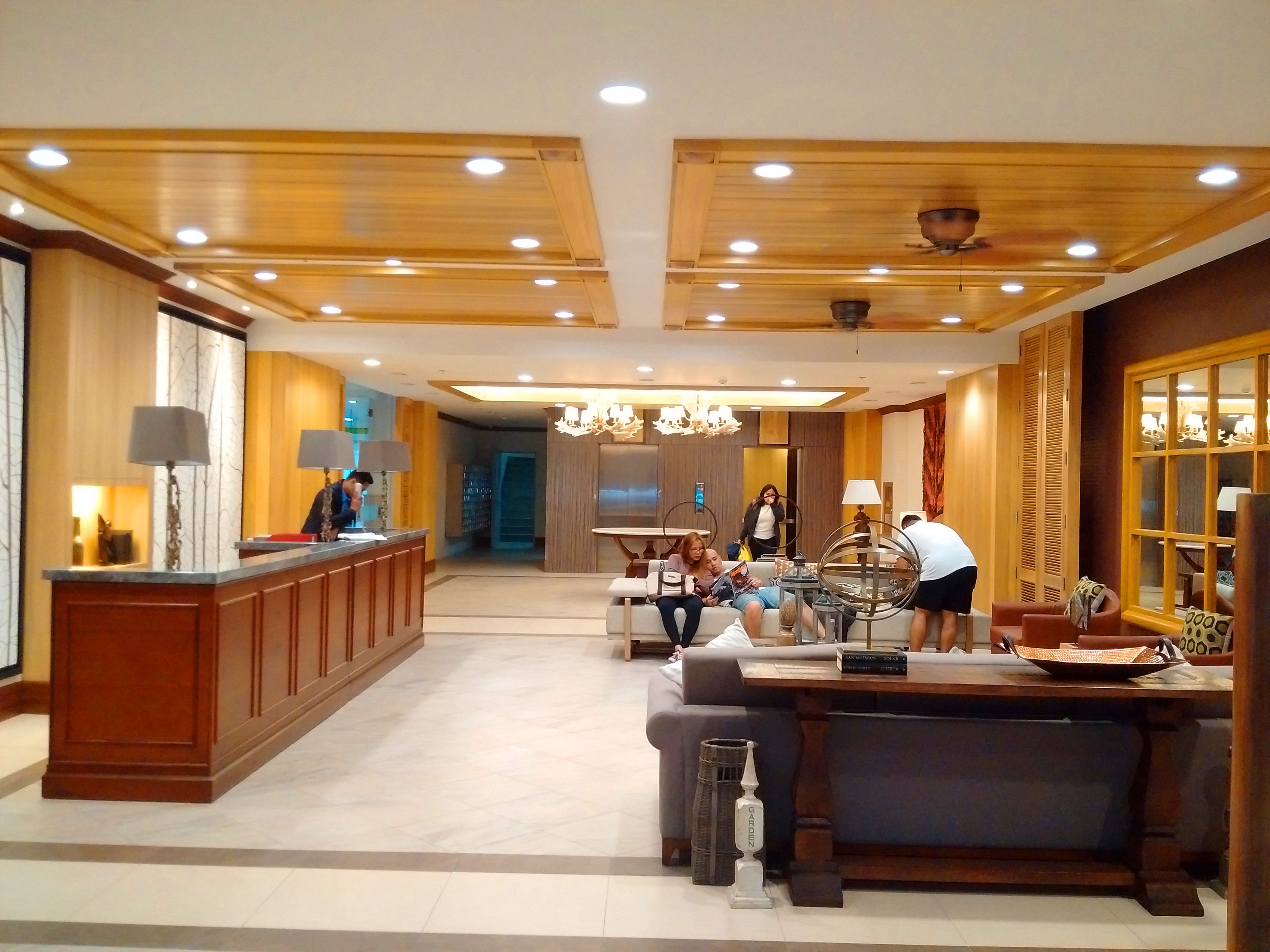 A spacious hotel lobby with a reception desk, seating area, and a large window.