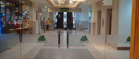 A hotel lobby with a modern design, featuring a central chandelier, patterned floor tiles, and glass doors with the hotel's logo.
