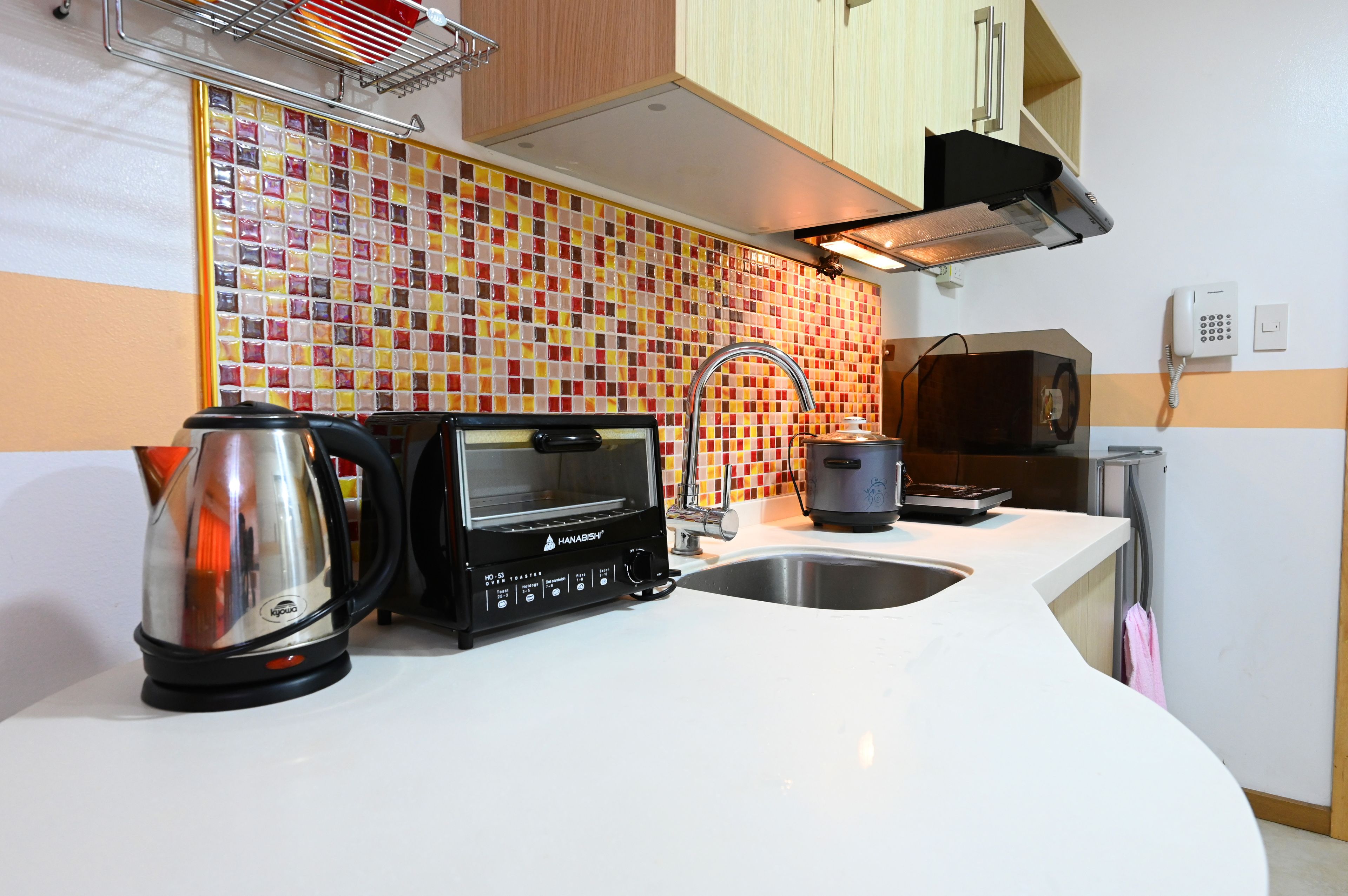 Una cucina moderna con forno a microonde, tostapane e bollitore sul piano di lavoro, zoccolo in piastrelle e lavello.