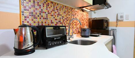 A modern kitchen with a microwave, toaster, and kettle on the counter, a tiled backsplash, and a sink.