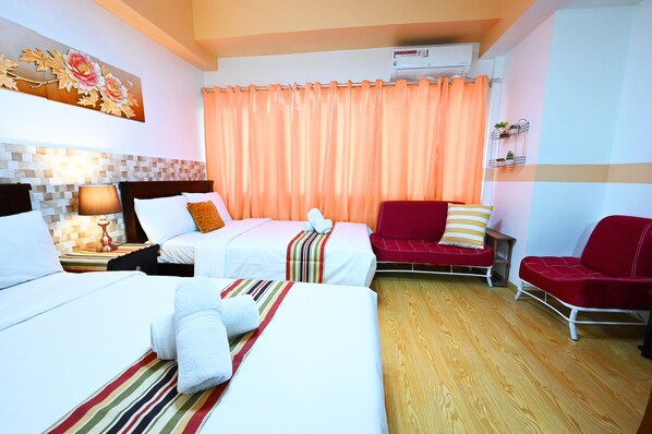 A hotel room with two beds, a red sofa, a small table, and a wall-mounted air conditioner.