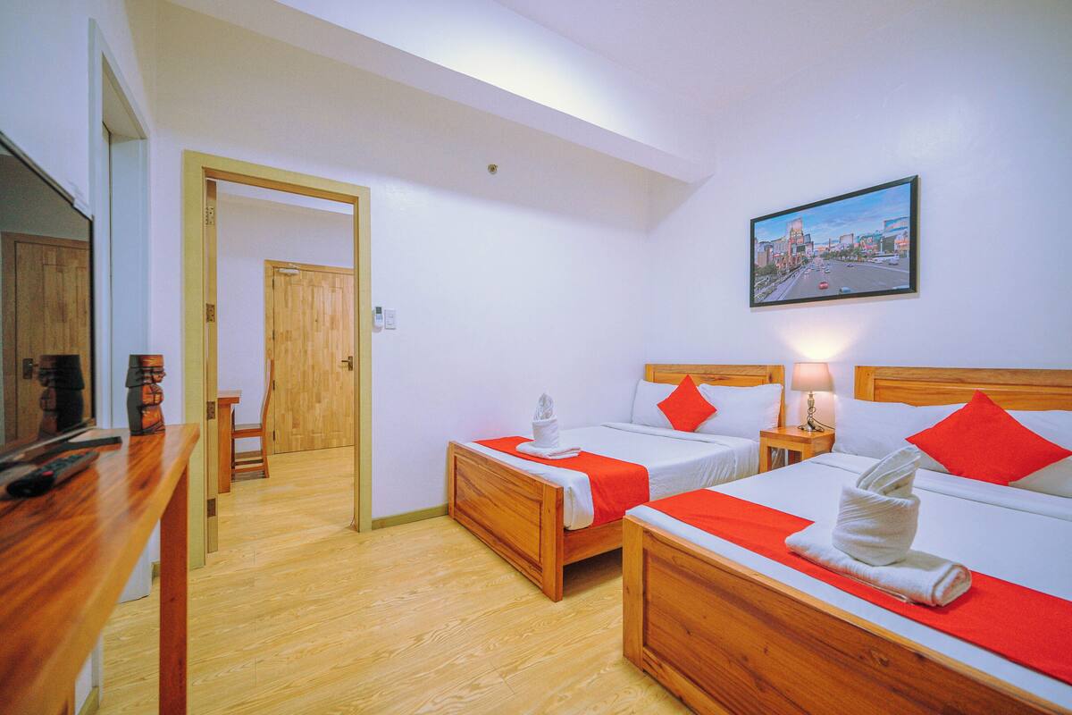 Habitación de hotel con dos camas de madera, un escritorio de madera, una silla y un cuadro en la pared.