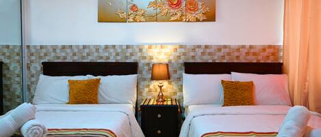 A hotel room with two beds, a nightstand with a lamp, a decorative wall piece, and a tiled backsplash.