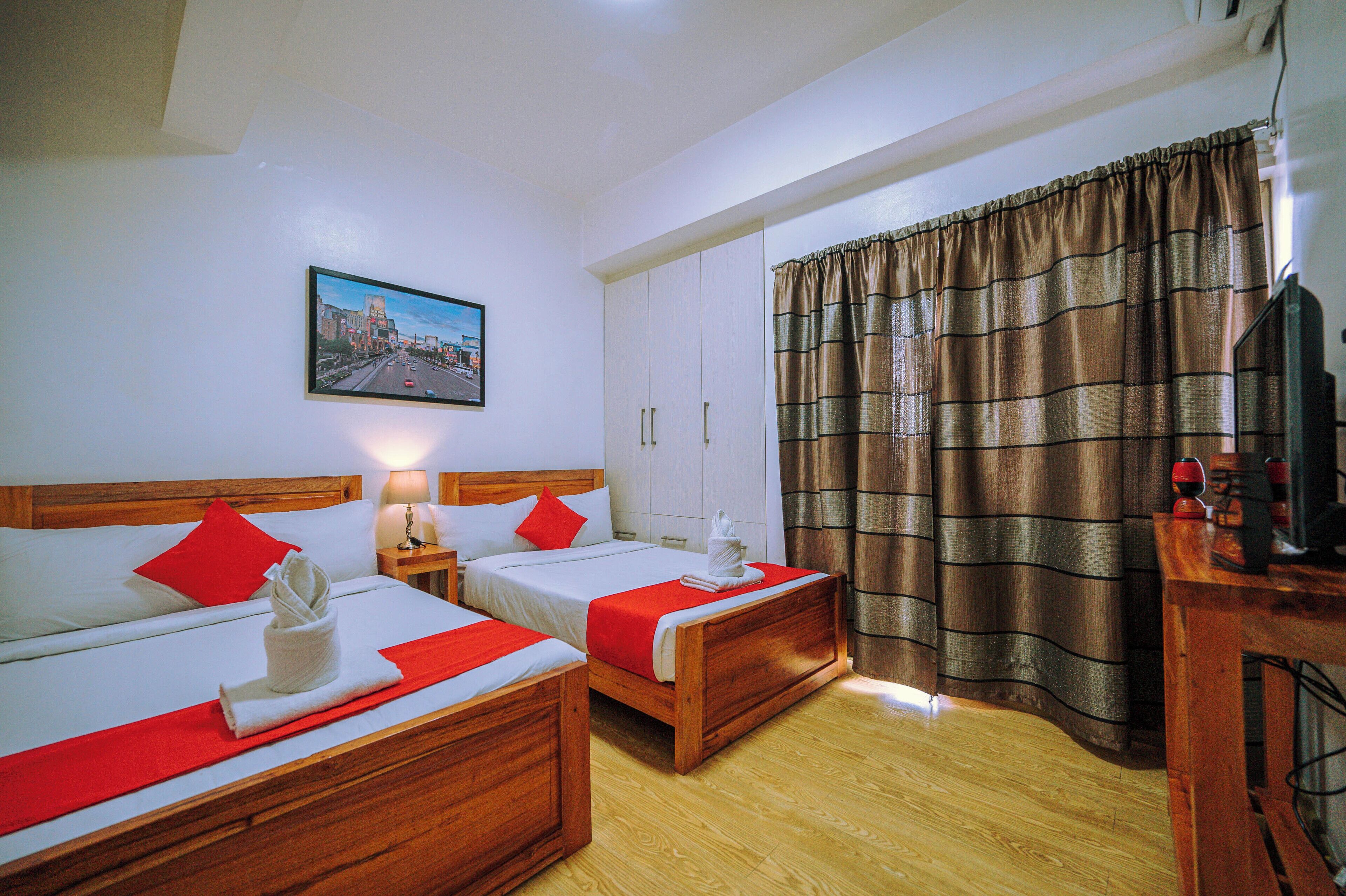 Une chambre d’hôtel avec deux lits, une tête de lit en bois, un tableau au mur et un rideau.