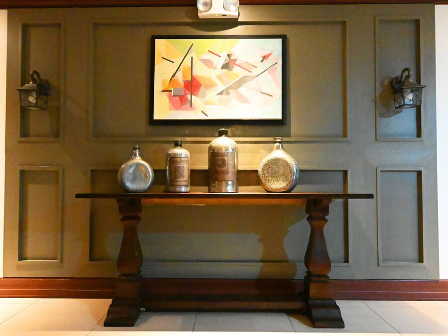 A reception area with a wooden console table displaying three bottles, a framed abstract painting, and two wall-mounted lanterns.