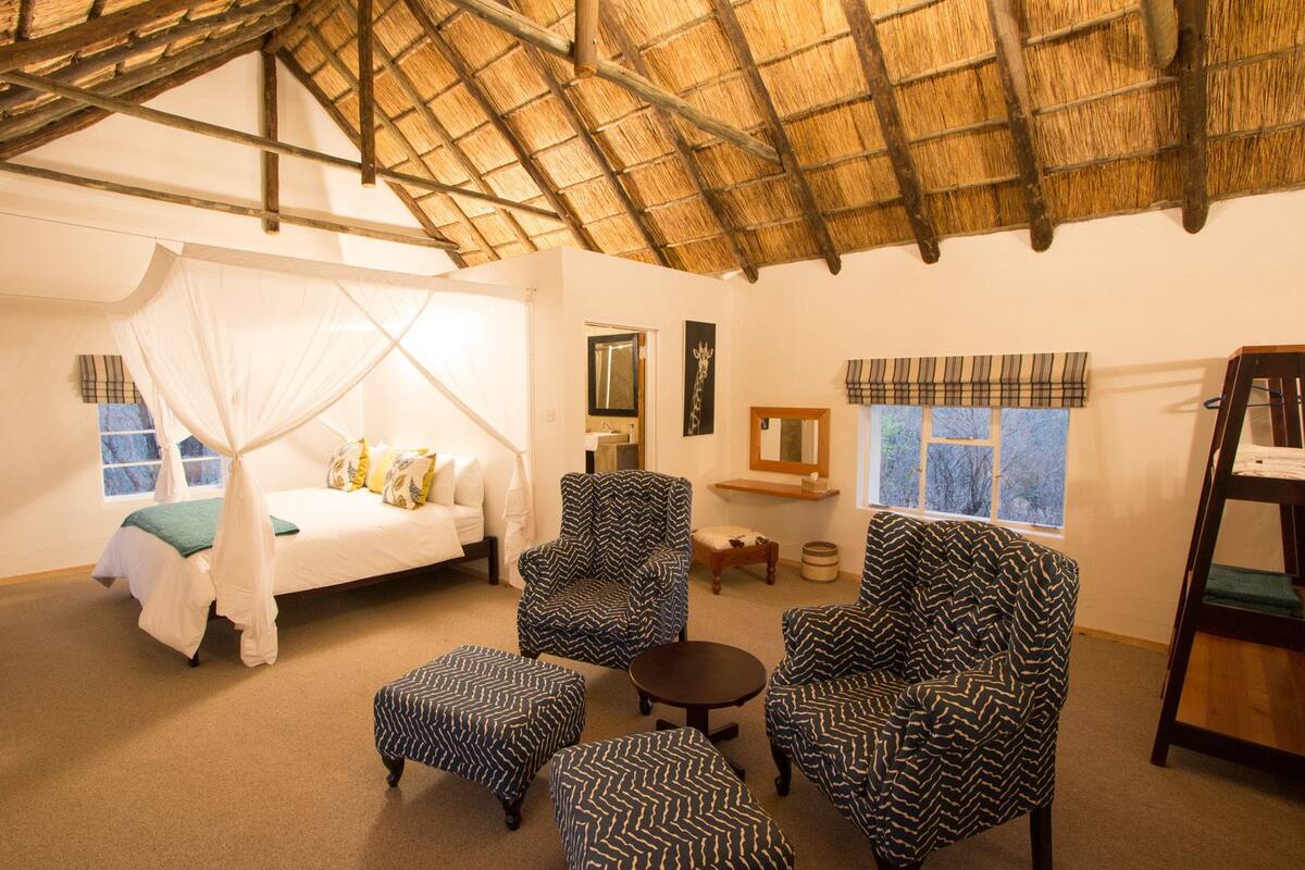 A room with a bed, two armchairs, a small table, and a bench.